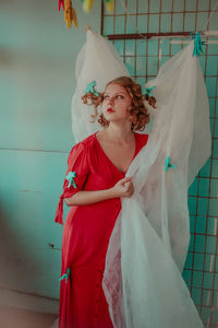 Thoughtful woman in red dress with curtain at home