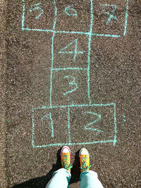 Lower section of a  child playing an old game called hopscotch on the street . 