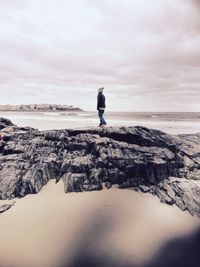 Boy standing on rocks at the ocean in winter 