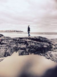 Boy standing on rocks at the ocean in winter 