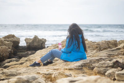 Rear view of woman sitting on rock at beach