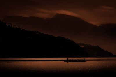 Silhouette mountain by sea against sky during sunset