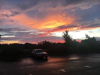 Cars on road against dramatic sky during sunset