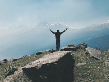 Rear view of man with arms raised standing on mountain against sky