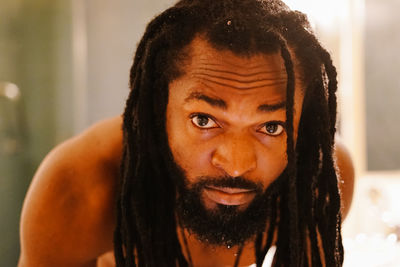 Close-up portrait of shirtless man with dreadlocks bending in bathroom