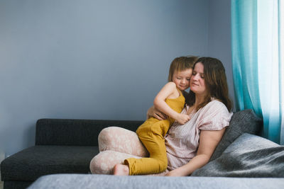 Plus, european mother hugs toddler child sitting on sofa in real interior of living room