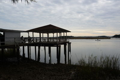 Stilt house in lake against sky during sunset