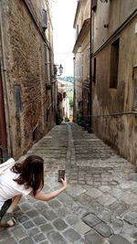 Rear view of woman photographing alley amidst buildings