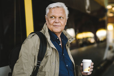 Contemplative senior businessman holding disposable cup at railroad station