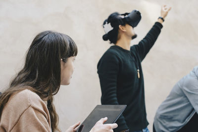 Male computer programmer gesturing while using vr glasses by colleagues in office