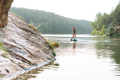 The young woman in green sweemsuit on sup boat with oar floating on river, weekend trip and travel