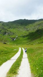 Man walking on road amidst field against sky