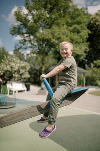 Full length side view portrait of happy boy with down syndrome sitting on seesaw at park