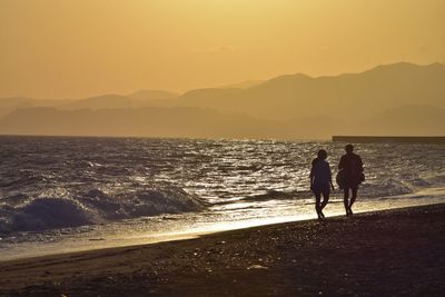 Silhouette people on beach against sky during sunset