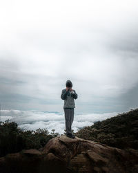 Rear view of man standing on rock against sky