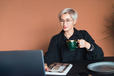 Fashion woman in black shirt working in modern work place or office with laptop and coffe cup