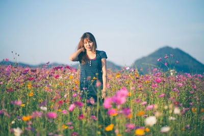 Woman standing by flowering plants on field against sky