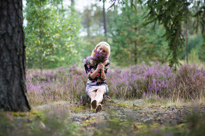 Woman looking away while holding flowers in forest