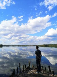 Rear view of man standing by lake against sky