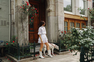 Rear view of woman standing with dog by building