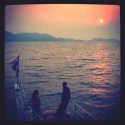 People on sea against sky during sunset