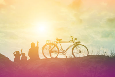 Silhouette people by bicycle against sky during sunset