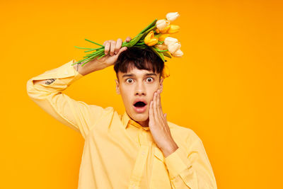 Portrait of young woman with arms raised against yellow background