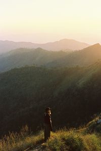 Rear view of woman walking on landscape against sky during sunset