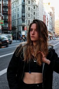 Beautiful young woman looking away while standing on street in city