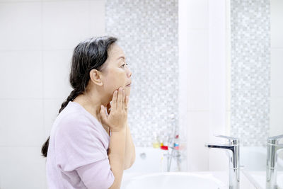 Side view of senior woman washing face in bathroom at home