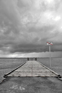 No swimming sign on pier by sea against cloudy sky