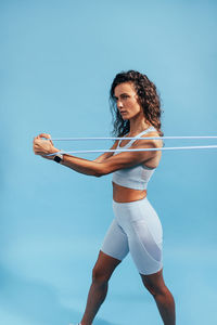 Woman stretching resistance band against blue background