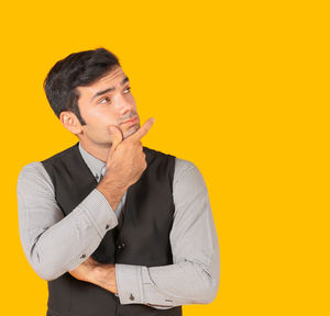 Man looking away while standing against yellow background