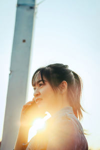 Portrait of young woman looking away against sky on sunny day