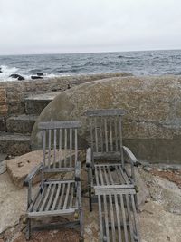 Empty chairs on beach against sky