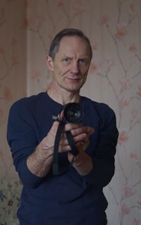 Portrait of mature man holding camera against wall