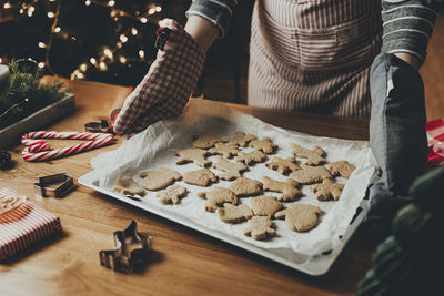 Young woman holds deco, holding sheet with ready-made baked gingerbread cookies in her gloves hands