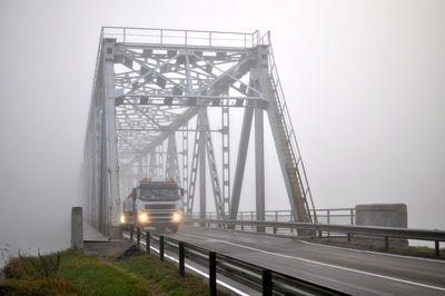 Truck moving on foggy bridge against sky