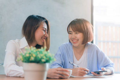 Portrait of a smiling young woman using phone while sitting on table