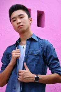 Portrait of young man standing against pink wall