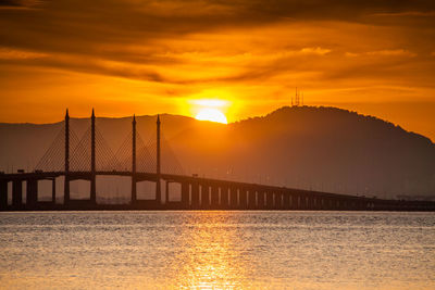 Bridge over sea against orange sky