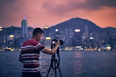 Man photographing river in city at dusk