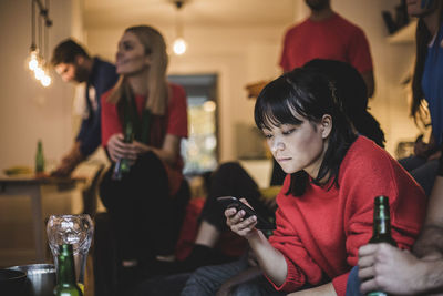 Young woman using mobile phone while sitting with friends at home