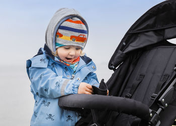 Cute girl playing with baby stroller against sky