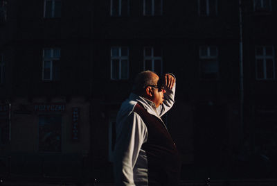 Side view of man photographing while standing against window at night