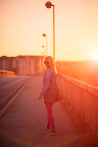 Rear view of woman walking on street against sky during sunset