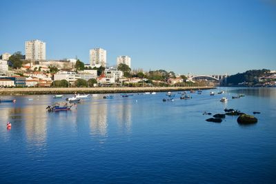 Boats in sea by buildings against clear blue sky