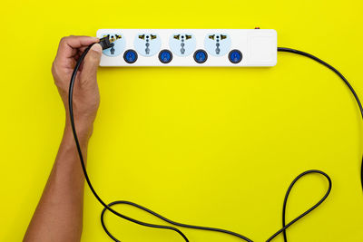 Cropped hand of woman putting cable in plug against yellow background