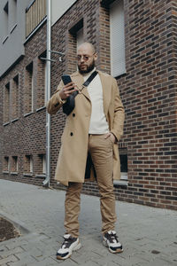 Full length of man holding phone standing against wall