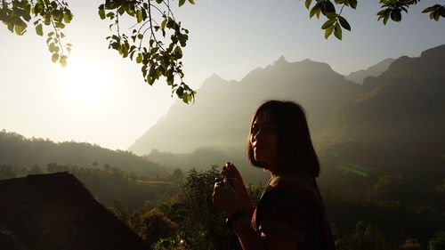 Portrait of woman holding coffee cup by mountains against sky